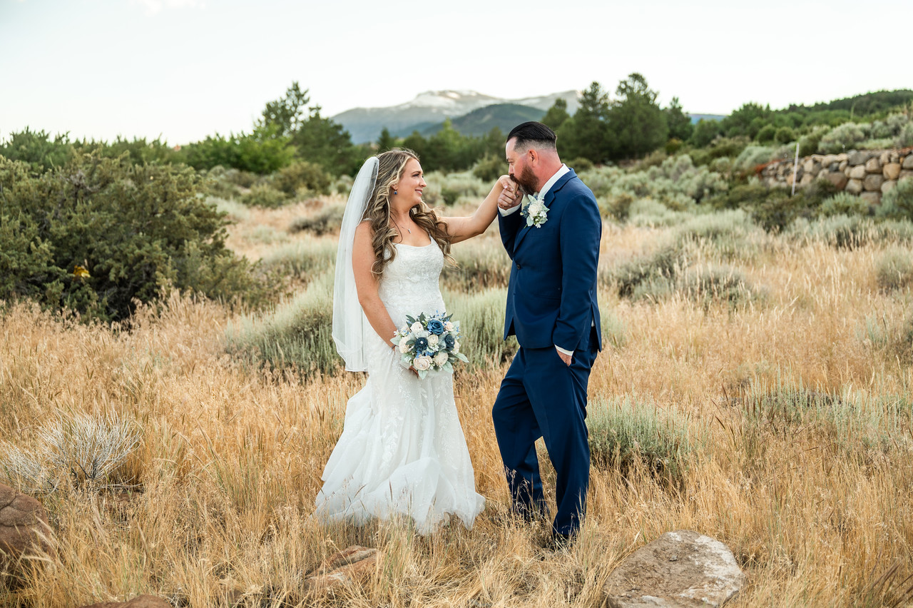 Bride holding a blue-and-white bouquet as the groom kisses her hand in a golden Sierra meadow