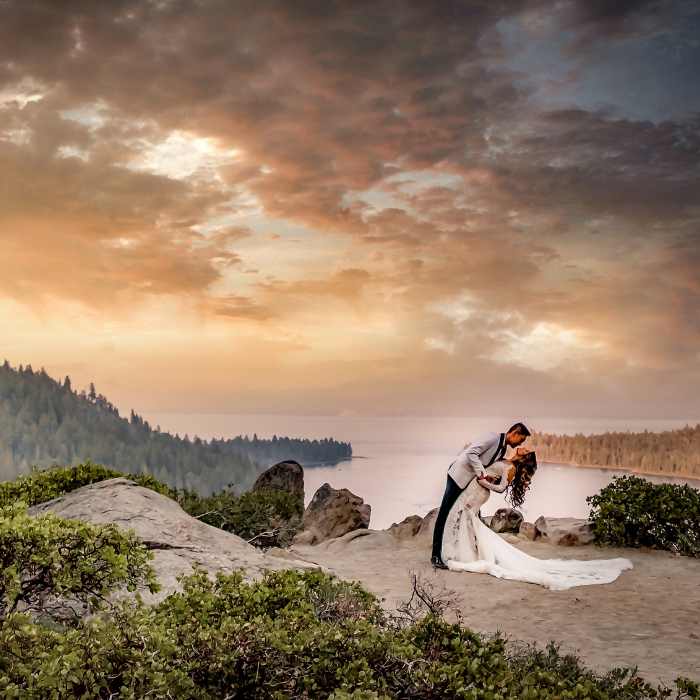 A groom dipping his bride for a kiss on a rocky overlook above Lake Tahoe at sunset